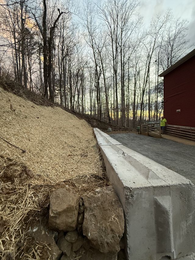 Precast concrete drainage channel with a freshly graded and straw-mulched slope at dusk, red barn in the background, western North Carolina