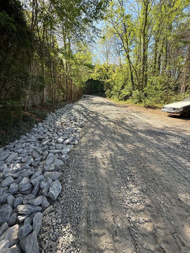 Gravel driveway with a riprap stone drainage channel through the woods