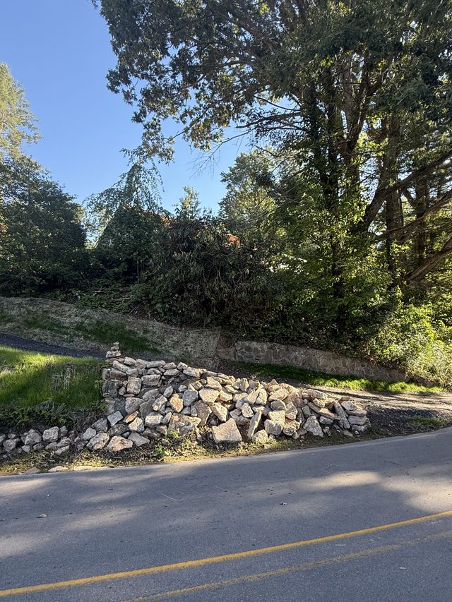 Close-up of a dry-stack fieldstone retaining wall along a graded roadside embankment in warm light