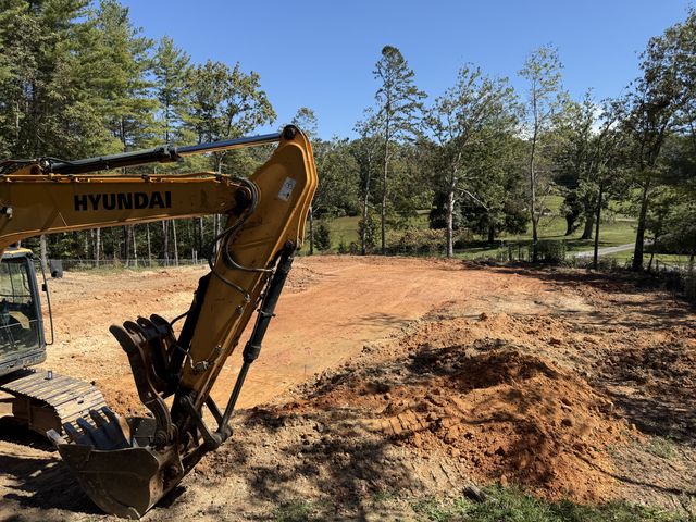Hyundai excavator arm and bucket in warm light over a graded building pad with rolling western North Carolina hills behind