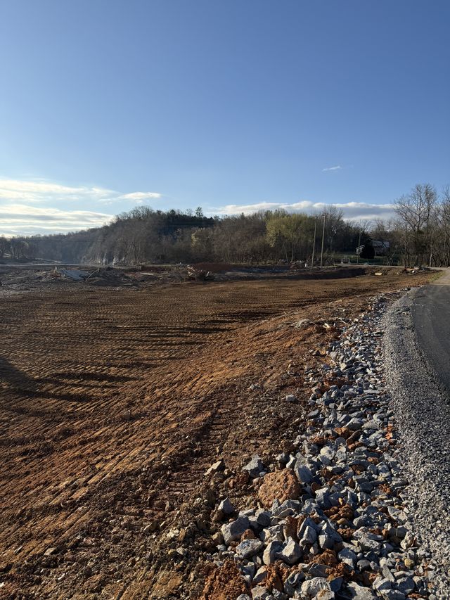 Freshly graded dirt pad edged with riprap stone along a gravel road under a blue sky, western North Carolina grading site