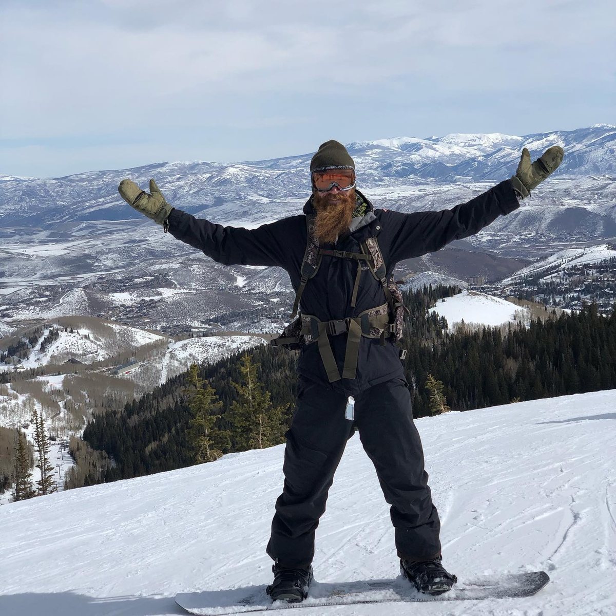 Jon Sprouse snowboarding on a mountain summit, arms spread wide